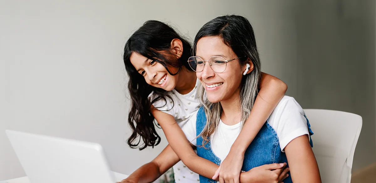 Una madre y su hija sonríen mientras utilizan el ordenador